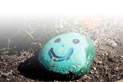 Stone painted green with a blue smily face