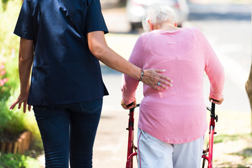 Nurse assists elderly woman walk outdoors