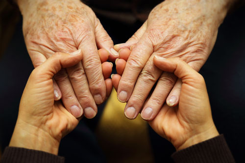 A young adult holds the hands of an older adult