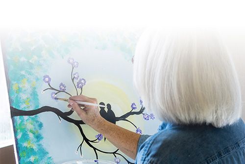 An elderly woman paints purple flowers
